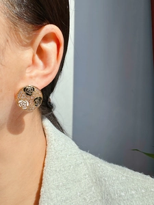 Close-up of a large round gold earring featuring black and white enamel flowers and crystals