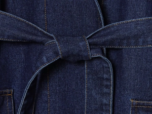 Détail macro du tissu denim bleu foncé avec coutures orange et ceinture à nouer à la taille