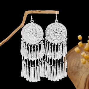 Detailed macro view of Bohemian silver tassel earrings with flower pattern on dark background