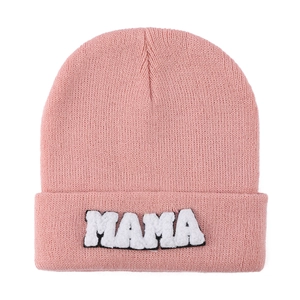 Close-up of pink knit beanie with MAMA towel embroidery on folded cuff against white background