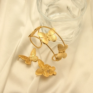 Chic 18k gold butterfly jewelry set featuring a cuff bracelet and stud earrings on silk
