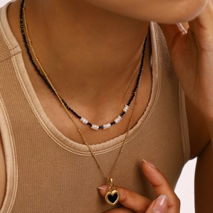 Detail of layered gold necklace with black heart pendant and pearl spinel beads