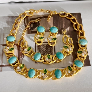 Vintage gold jewelry set with turquoise, emerald gems, and pearls on editorial background