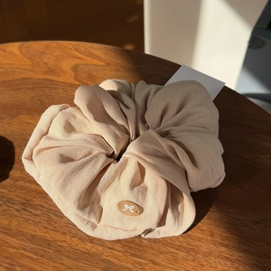 Detail of cream scrunchie with linen texture and amber oval bow emblem on wood