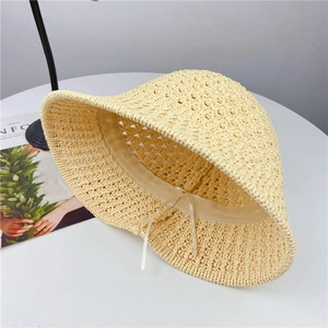 Handwoven beige hollow straw bucket hat with delicate ribbon on a clean aesthetic desk