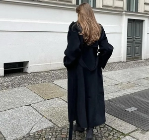 Vue arrière d'un long manteau en laine noir avec ceinture et silhouette minimaliste élégante