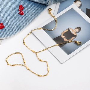 Details des verstellbaren goldenen Gliederarmbands mit Zylinderanhängern auf Denim-Stoff