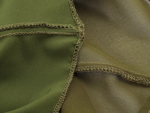 Close-up of overlock stitching and pleated chiffon fabric texture on a green dress