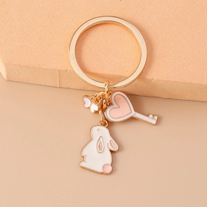 Detail of a golden metal keychain featuring white enamel rabbit and heart key pendants