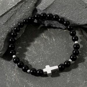 Black matte onyx beaded bracelet with silver cross pendant on natural stone surface