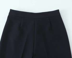 Detail of high-waisted black crepe trousers featuring front pleats and tailored waistline