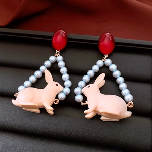 Close-up of cute pink rabbit pendant earrings with red beads and blue pearl strands