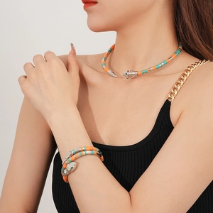 Close-up of snake-shaped necklace and coiled bracelet with colorful beads and green gem eyes