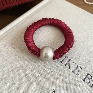 Elegant burgundy satin scrunchie with large pearl detail on a cream book background