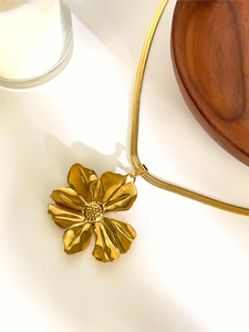 Macro detail of a large golden flower pendant featuring a sleek snake bone chain texture