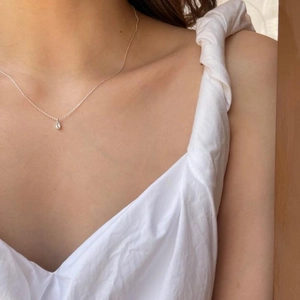 Close-up of a minimalist silver teardrop pendant necklace on a model's collarbone