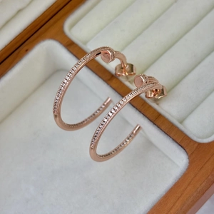 Dettaglio di orecchini a C in oro rosa con zirconi in una scatola per gioielli beige