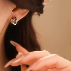 Vue détaillée de boucles d'oreilles nœuds en métal argenté portées avec lumière douce