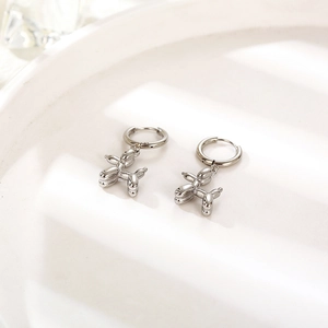 Detailed view of silver balloon dog earrings on a white ceramic tray with soft shadows