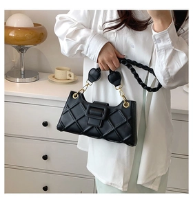 Detail of black quilted shoulder bag with woven strap shown in a modern home interior