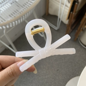 Close-up of a translucent white bow hair clip with a gold spring held by hand