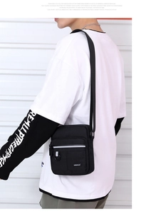 Rear view of a black oxford fabric crossbody bag with reflective strips and adjustable strap