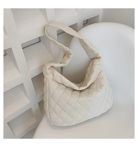 Close-up of white quilted puffy shoulder bag with soft padding on a minimalist chair