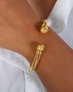 Dettaglio di un bracciale a polsino intrecciato dorato con estremità a sfera al polso