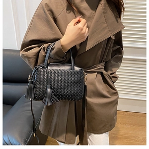 Detail of black woven leather handbag with tassels worn with a brown trench coat