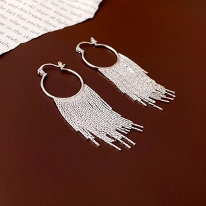 Détail de boucles d'oreilles créoles argentées avec de longs glands métalliques