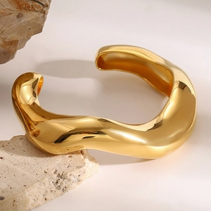 Minimalistischer goldener wellenförmiger Armreif auf einem natürlichen Rohsteinpodest