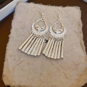 Detailed shot of silver hollow patterned earrings with long flowing fringe tassels