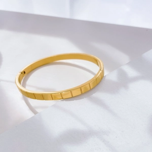 Detailed view of golden minimalist bangle with vertical rectangular engraved texture