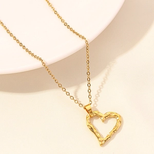 Macro shot of gold heart necklace with hammered texture on a white porcelain dish