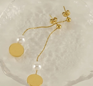 Macro detail of gold tassel earrings with snake chain and white pearl on glass