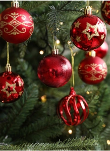 Close-up of assorted red and gold Christmas baubles hanging on a pine tree with warm lights