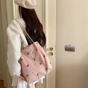 Detail of pink corduroy tote bag featuring bear embroidery and metal snap button closure