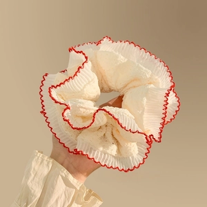 Detail of white lace scrunchie with red pleated edges held in hand on beige background