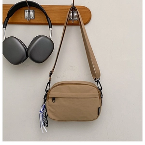 Détail du sac bandoulière en nylon kaki avec nœud tressé et poche zippée noire