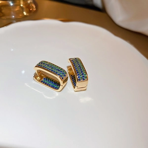 Detail of gold geometric earrings with pavé blue and green zircon stones on white tray