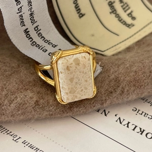 Retro gold ring with rectangular beige textured stone on a soft brown fabric background