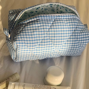 Blue and white checkered quilted makeup bag made of cotton on soft bedding background