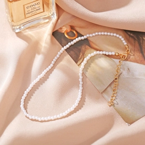 Detail of elegant white pearl necklace with golden lobster clasp on pink silk