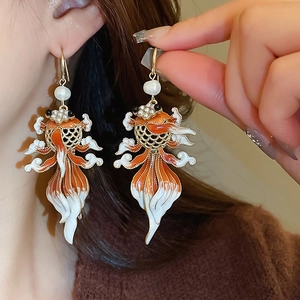 Close-up of goldfish drop earrings featuring enamel detailing and white pearls on ear