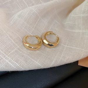 Detailed close-up of golden geometric hoop earrings resting on a beige linen fabric surface