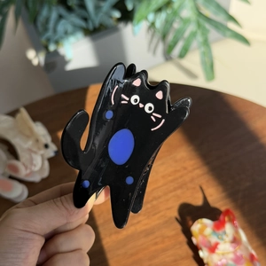 Gros plan d'une pince à cheveux chat noir en acétate avec pois bleus et détails roses