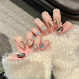 Faux ongles faits main bleu œil de chat avec feuilles d'or et strass sur pull blanc