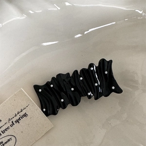 Detailed view of black wavy hair clip with white polka dots on soft textured background