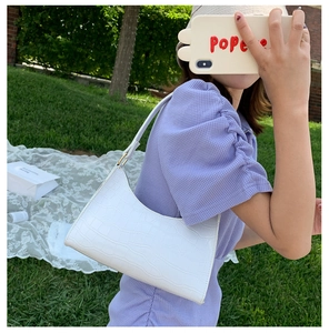 Close-up of white crocodile pattern shoulder bag held by model in outdoor natural light