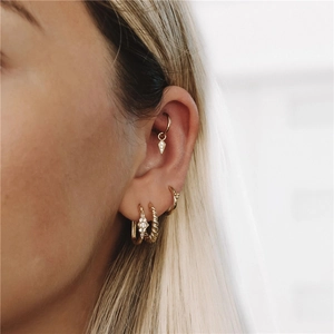 Close-up of stacked gold petal earrings and zircon studs on a model's ear